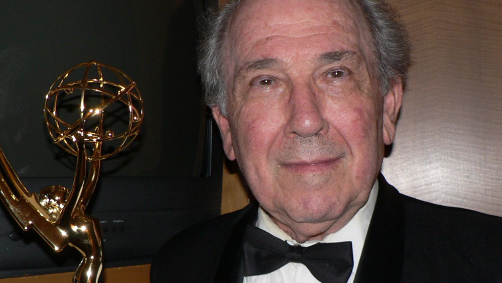 Filmmaker Robert Richter looks at the camera with a slight smile_ wearing a black tux. A gold Emmy statue is to his left.