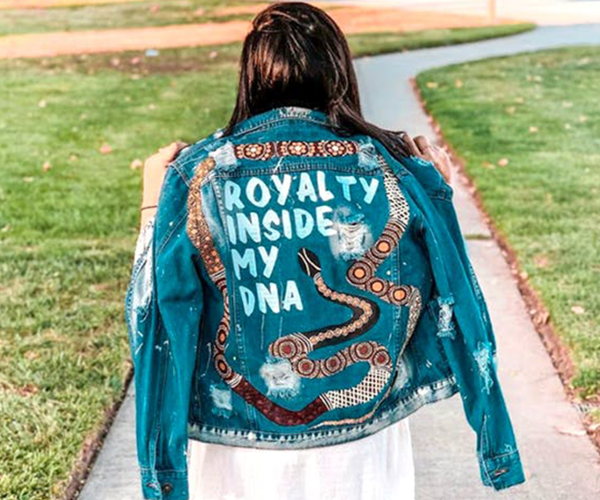 A girl wearing a denim jacket adorned with Aboriginal art and the words "Royalty inside my DNA"