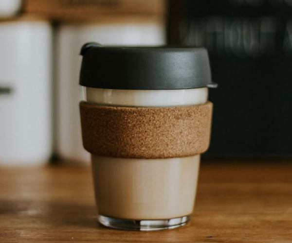 A keepcup filled with a milky coffee sits on a wooden bench