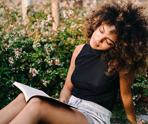 A girl with curly hair sits outside reading a book