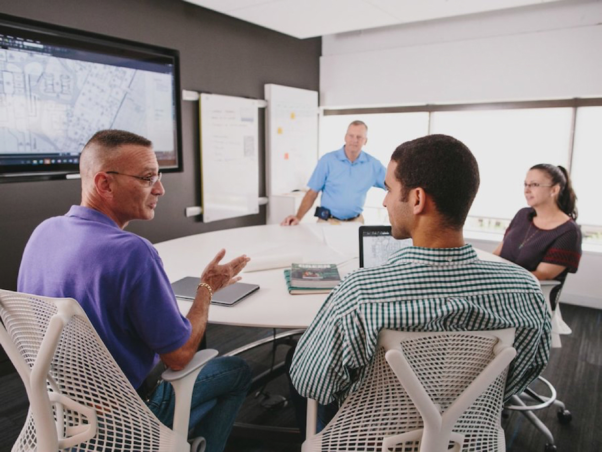 Four people meeting around a conference table with a large monitor on the wall