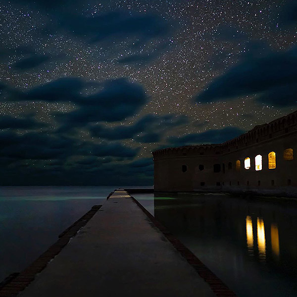 nighttime picture of part of fort jefferson with light coming from three openings, part of the moat and the ocean