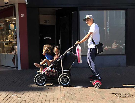 dad pushes double stroller while on hoverboard