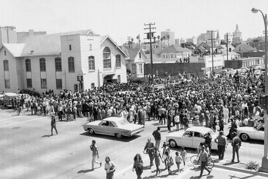 Black August. Black and white photo of funeral procession of 17-year-old Jonathan Jackson, flanked by Black Panther Party members raising the Black Power salute. 
