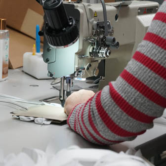 A person with a grey and red sweater working at a sewing machine