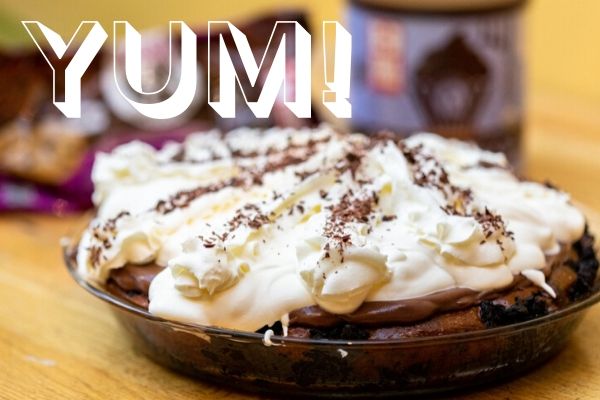 A pie covered with whipped cream and chocolate, with the word "Yum!"