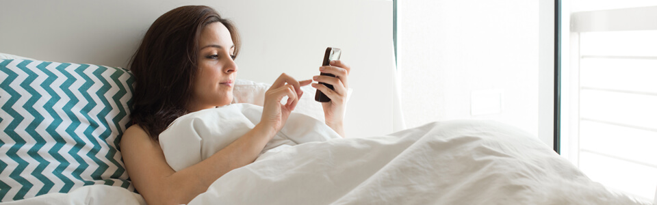 woman in bed, looking at her phone 