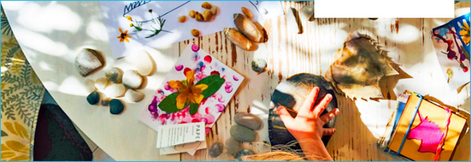 Clickable image of a child''s hand on a table full of craft materials.