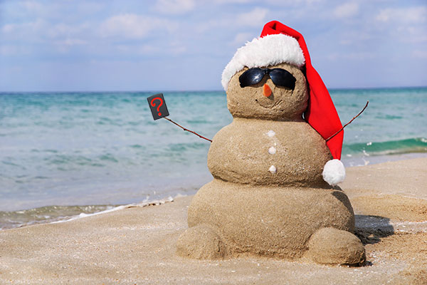 snowman made of sand on beach with santa hat and sunglasses holding a mystery design Zippo lighter.