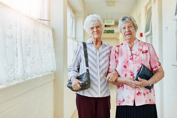 Two women in their 90s carrying purses and leaving for an excursion at their nursing home.