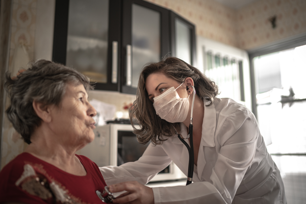 Medical professional wearing a facemask cares for an elderly woman.
