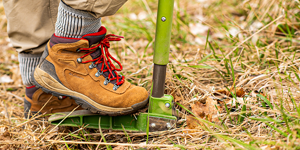 Volunteer in hiking boots using a green garden tool.