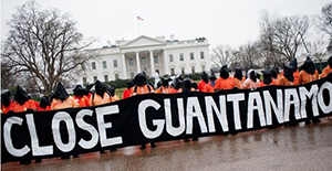 a crowd of protesters holds a banner that reads close guantanamo