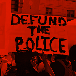 a protestor holds a sign that reads defund the police in large bold lettering