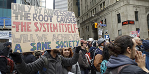 a protester holds a sign reading only by addressing the root causes the system itself will we achieve a safe society